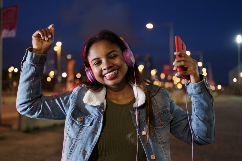 Young African American Latin Woman listening to salsa music on headphones and smartphone in the city at night