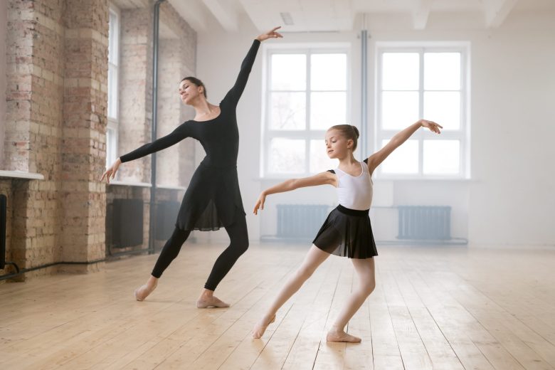Little ballering girl dancing together with her trainer during classes in dance studio